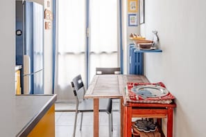 A kitchen with a wooden table, chairs, and a small shelf with kitchenware. - The apartment welcomes guests into a warm, colorful, and personality-filled environment, designed to offer maximum livability and relaxation during your stay.The living area is the heart of the home: a large, bright living room where guests can gather to (Torino)
