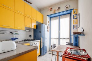 A kitchen with yellow cabinets, a white toaster, a blue refrigerator, and a dining table with a red tablecloth. - Bright four-room apartment with large terrace (Torino)