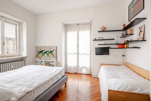 A room with two beds, a radiator, a window, a painting, and a TV on a shelf. - Bright four-room apartment with large terrace (Torino)