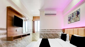 A hotel room with a bed, a flat-screen TV, an air conditioning unit, a marble wall, and a window with curtains. - Super Collection O Ahmedabad Airport (Ahmedabad)