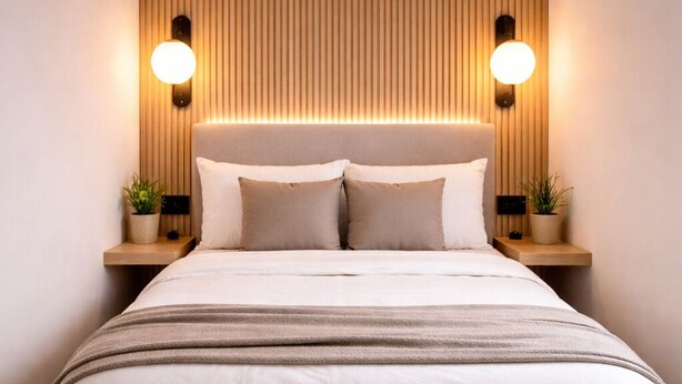 Ein modernes Schlafzimmer mit einem großen Bett, einem Holz-Kopfteil, Nachttischlampen und einer kleinen Pflanze auf dem Nachttisch.