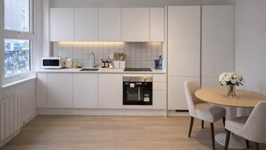 Eine moderne Küche mit weißen Schränken, einem eingebauten Backofen und einem Essbereich mit einem runden Tisch und Stühlen.