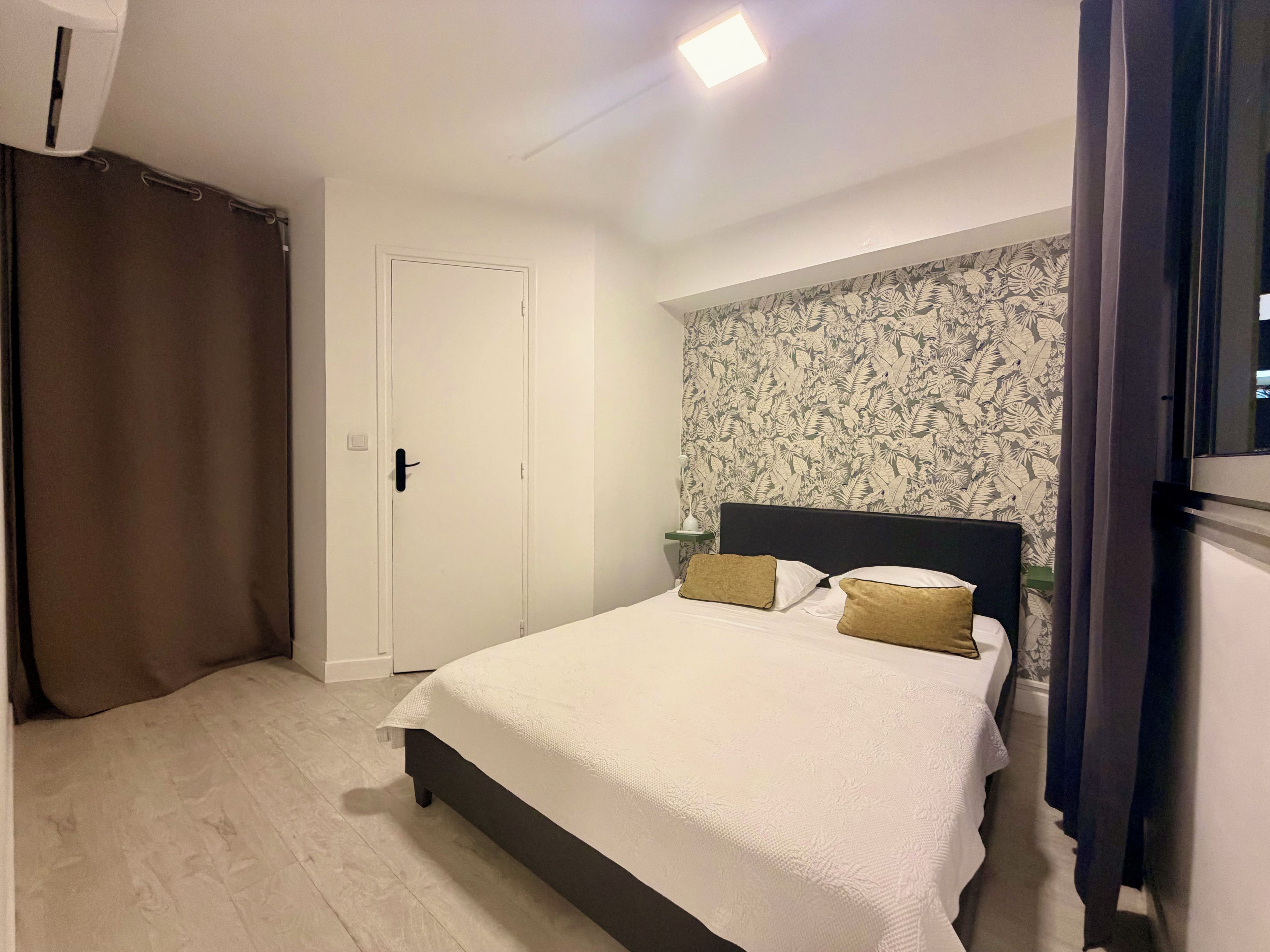 Un dormitorio con cama, cortinas, una puerta y una pared con estampado floral.