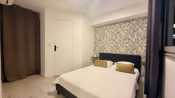 Un dormitorio con cama, cortinas, una puerta y una pared con estampado floral.
