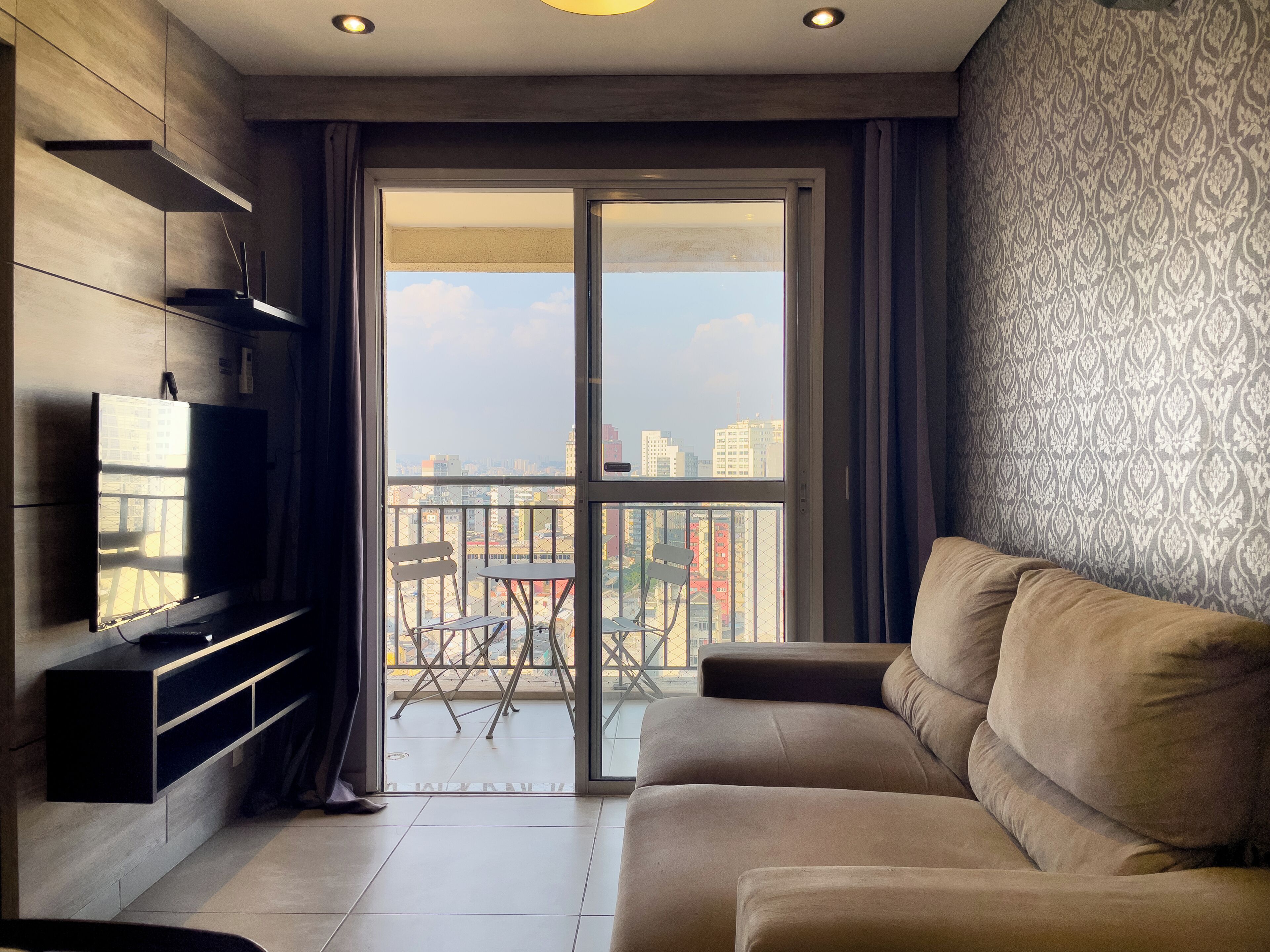 Una sala de estar moderna con un sofá, un televisor y un balcón con vista a la ciudad.