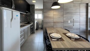 A modern kitchen with a built-in refrigerator, a stove, and a dining area with a wooden table set for two. - SP New Home (São Paulo)