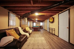 A room with a pool table, a sofa, a door, and a sign for vacation rentals. - Misty Mountain Cottage - Pet Friendly (Shippen Township)