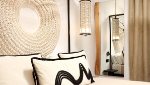 Ein Schlafzimmer mit einem großen, runden, gewebten Kopfteil, einer Nachttischlampe, einem Spiegel und einem Bett mit zwei Kissen.