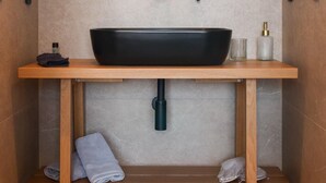 Ein Badezimmer mit Holzwaschtisch, einem schwarzen Hängebecken, einem Spiegel und einem Handtuchhalter.
