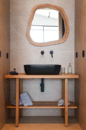 A bathroom with a wooden vanity, a black vessel sink, a mirror, and a towel rack.