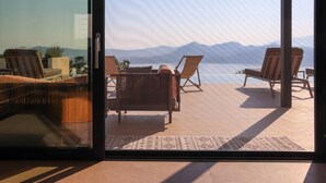Ein Zimmer mit Glastür und Zugang zu einer Terrasse, auf der sich zwei Holzstühle und ein Korbsessel befinden.