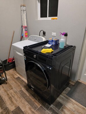 Ein Waschraum mit einer schwarzen Waschmaschine, einem Trockner, einem Mop und Reinigungsmitteln.