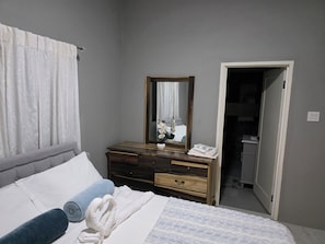 A bedroom with a bed, a dresser, a mirror, and a door leading to a bathroom.