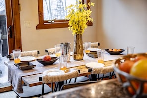 A dining table set with plates, glasses, a vase with yellow flowers, and a bowl of fruit. - Trailhead Basecamp • Ski/Bike‑In/Out • Hot Tub (Breckenridge)