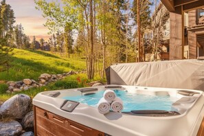 A hot tub with three rolled towels, surrounded by a grassy area with trees and a building in the background. - Ski/bike‑in/out • hot tub • mid‑mountain retreat (Breckenridge)