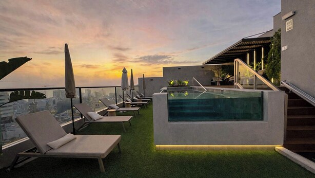 A rooftop pool area with lounge chairs and a view of the city skyline at sunset. - Luxurious brand-new apartment just a few blocks from Larcomar (Miraflores)