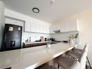 A modern kitchen with white cabinets, a black refrigerator, a marble countertop, and a small island with chairs. - Luxurious brand-new apartment just a few blocks from Larcomar (Miraflores)