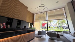 A modern reception area with a wooden reception desk, seating area, and large windows offering a view of the street. - Luxurious brand-new apartment just a few blocks from Larcomar (Miraflores)