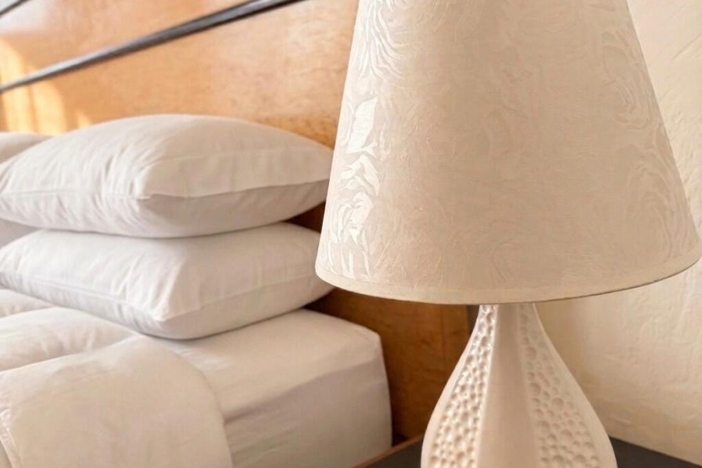 A bed with white pillows and a textured lamp.
