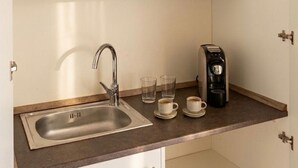Une cuisine équipée d’un évier en acier inoxydable, d’une machine à café et de deux tasses posées sur le comptoir.