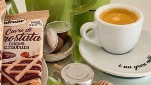 Une tasse à café posée sur une soucoupe, avec une assiette en dessous, une bouilloire verte, un petit bol et un paquet de biscuits secs.
