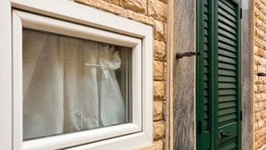 Une fenêtre avec un cadre blanc et un rideau, une porte à volets verts et un mur en pierre.