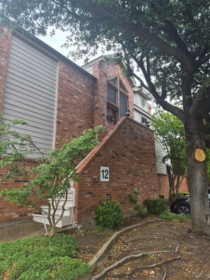 Un edificio de ladrillo con un letrero con el número 12, un pequeño porche y un árbol en primer plano.