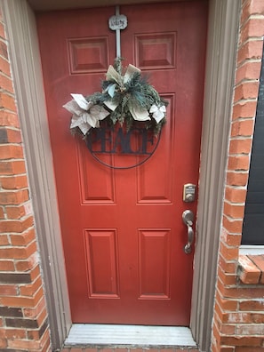Une porte rouge avec une pancarte « Bienvenue » et un symbole de la paix au-dessus.