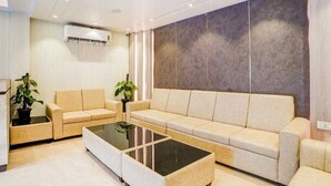 Una sala moderna con un sofá color beige, una mesa de centro de vidrio y dos plantas en macetas.