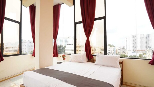 Habitación de hotel con una cama grande, cortinas rojas, vista a la ciudad y un ventanal con cortina.
