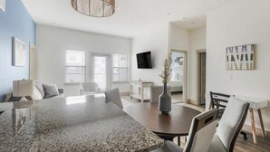 A modern living room with a dining area, a flat-screen TV, and a large window with blinds. - Landing Apartments Near Texas Children's Hospital West Campus (Houston)