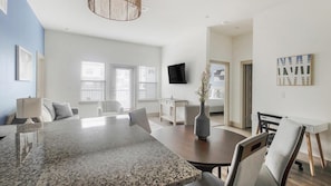 A modern living room with a dining area, a flat-screen TV mounted on the wall, and a large window with blinds. - Landing Apartments Near Texas Children's Hospital West Campus (Houston)