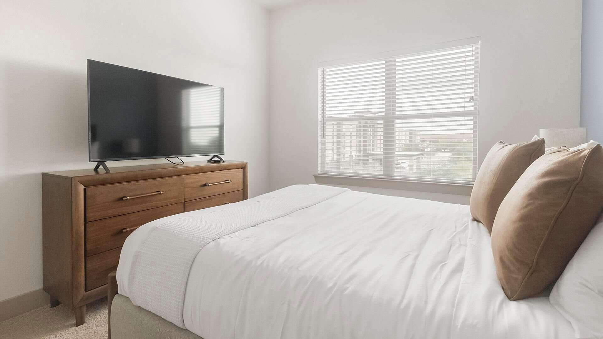 A bedroom with a bed, a dresser, a TV, and a window with blinds.