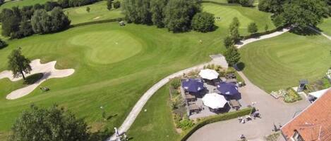 An aerial view of a golf course with sand bunkers, a clubhouse, and surrounding greenery.