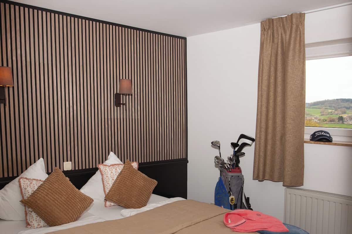 Une chambre d’hôtel avec un lit, des oreillers, un sac de golf et une vue sur la campagne.