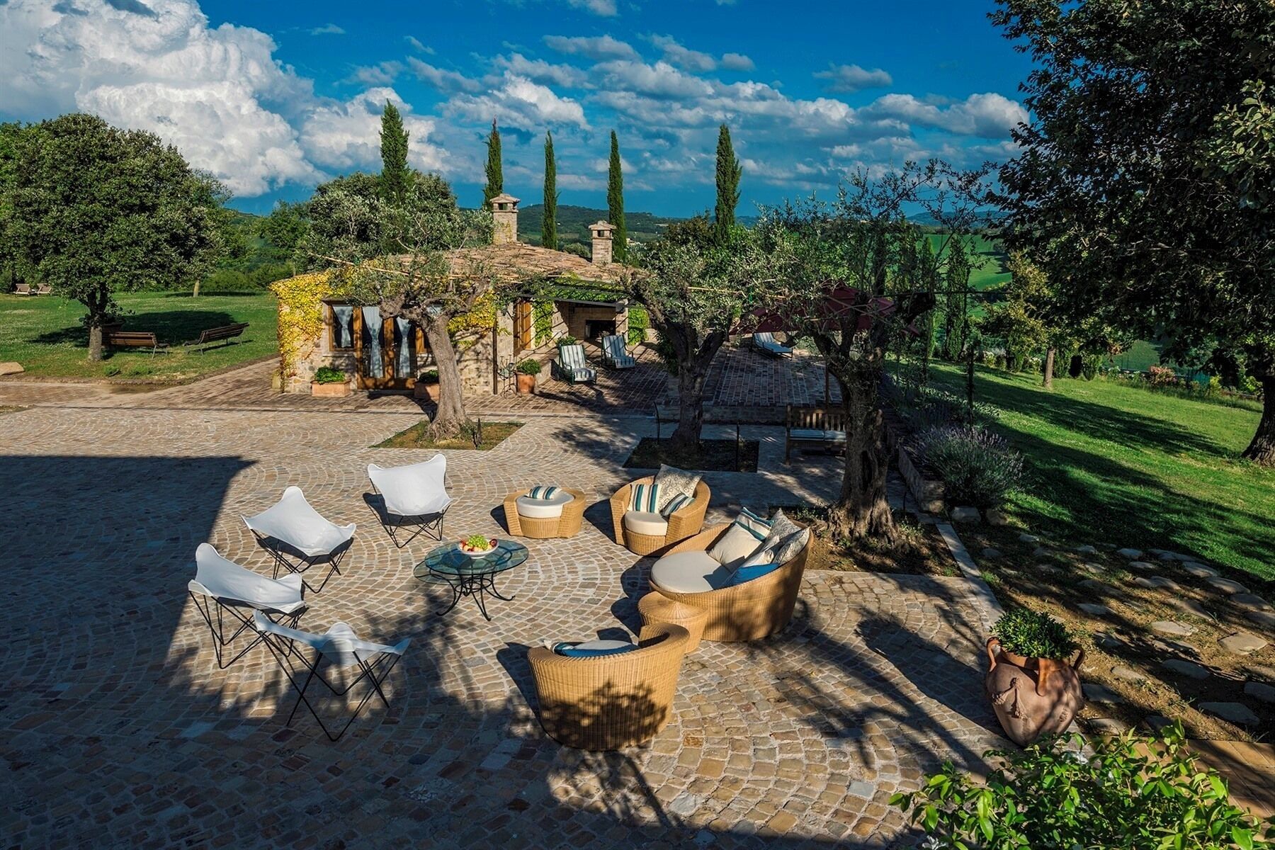 A courtyard with stone flooring, outdoor seating, and a stone building with a chimney.