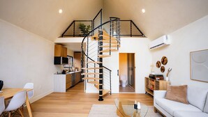 A spacious living area with a spiral staircase, a dining table with chairs, a sofa, and a kitchen in the background. - Getaway Cabin Retreat in Shenandoah Valley - Hot Tub, Sauna, Cold Plunge (Shenandoah Farms)