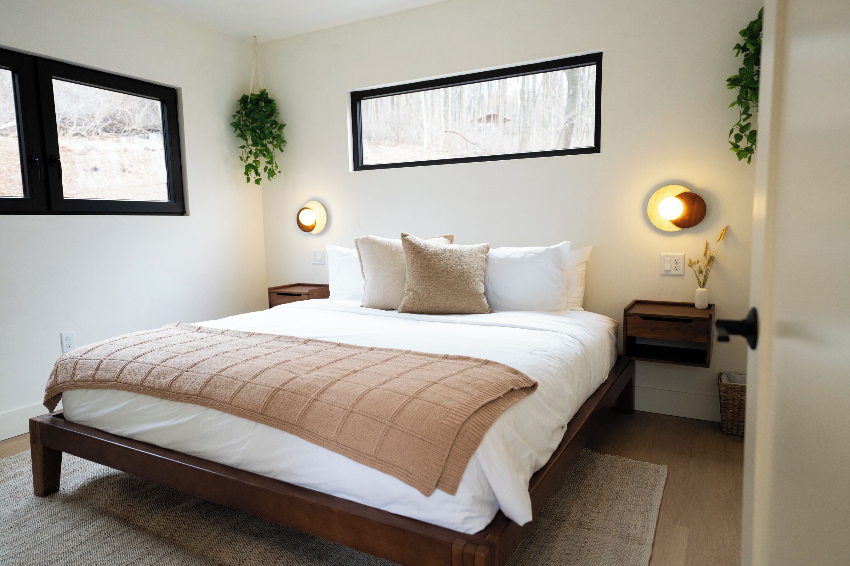 A bedroom with a bed, two bedside tables, a window, and wall-mounted lighting.