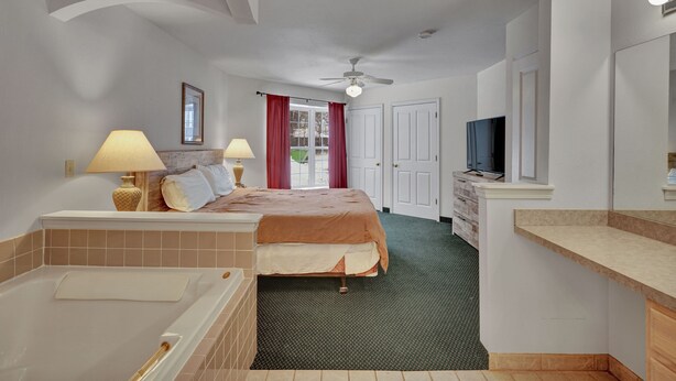 Ein Hotelzimmer mit Bett, Badezimmer mit Badewanne, Deckenventilator und Fernseher.
