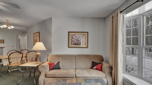 Ein Wohnzimmer mit einer Couch, Sesseln, einem Tisch und einem Fenster mit Vorhängen.