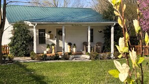 A single-story house with a green metal roof, a front porch with a bench, and a well-maintained lawn. - Cozy 4-bedroom cottage + tiny house in walkable to downtown Franklin with sauna (Franklin)