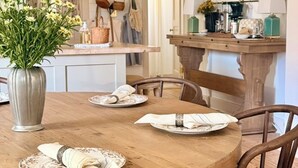A dining area with a wooden table set for four, chairs, a vase with flowers, and a kitchen in the background. - Cozy 4-bedroom cottage + tiny house in walkable to downtown Franklin with sauna (Franklin)