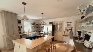 A kitchen with a central island, wooden stools, a stove, and various kitchen appliances. - Cozy 4-bedroom cottage + tiny house in walkable to downtown Franklin with sauna (Franklin)