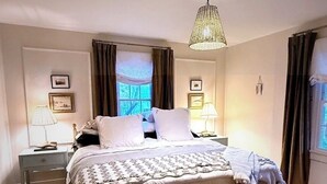 A bedroom with a bed, two bedside tables, a hanging light fixture, and a window with curtains. - Cozy 4-bedroom cottage + tiny house in walkable to downtown Franklin with sauna (Franklin)