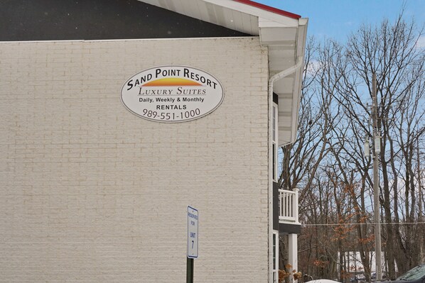 A building with a sign for Sand Point Resort, indicating it offers luxury suites with daily, weekly, and monthly rentals.