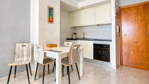 A dining area with a white table and chairs, a kitchen with white cabinets, and a wooden door. - Apartment 'Rosa De Los Vientos' with Sea View, Wi-Fi, and Air Conditioning (Calpe)
