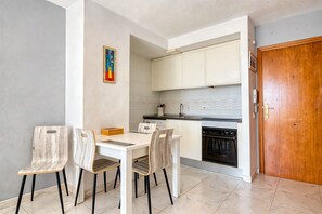 A dining area with a white table and chairs, a kitchen with white cabinets, and a wooden door. - Apartment 'Rosa De Los Vientos' with Sea View, Wi-Fi, and Air Conditioning (Calpe)