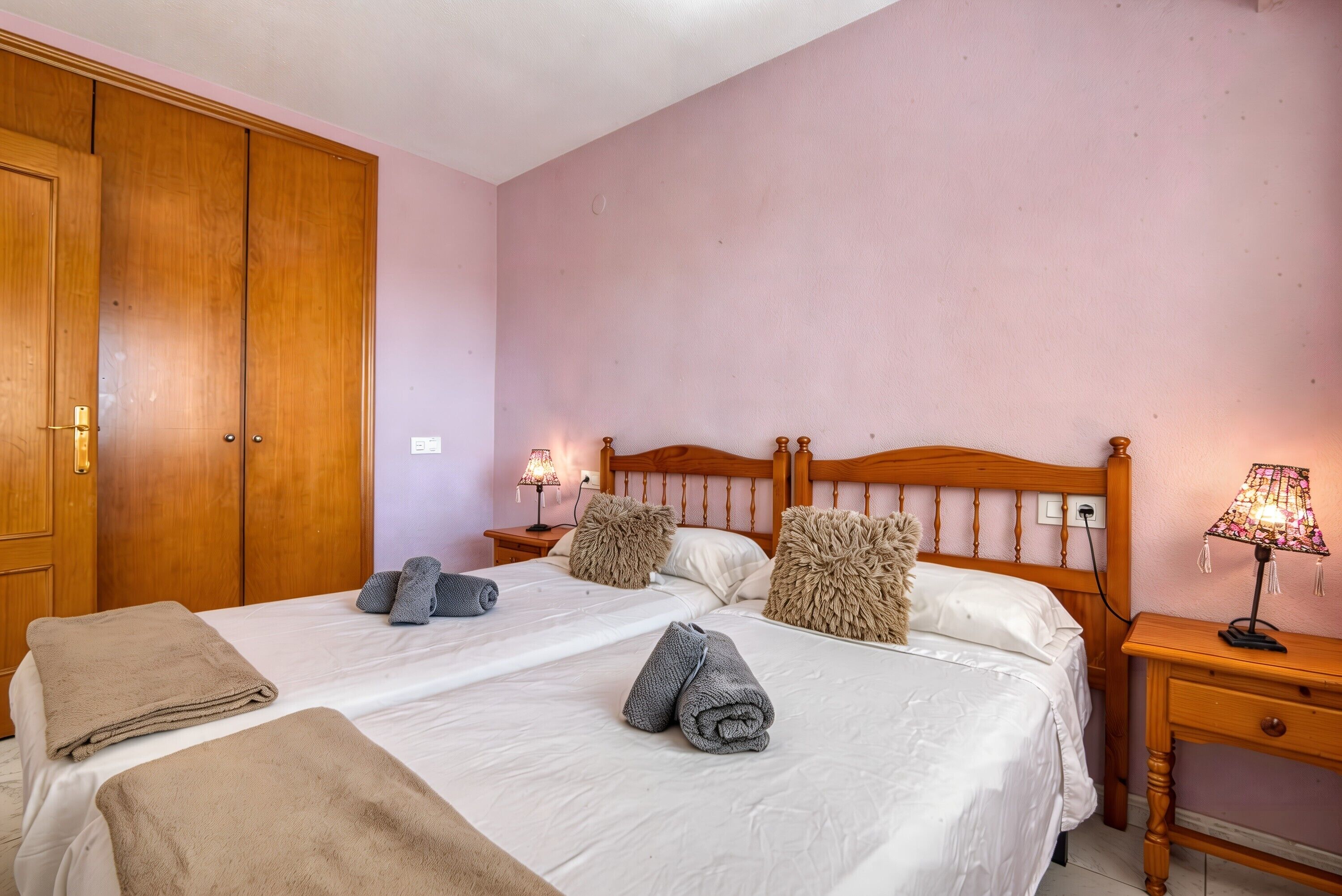 Un letto matrimoniale con due cuscini, un comodino con una lampada e un armadio in legno.