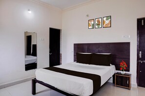 A hotel room with a bed, a mirror, a small bedside table, and three framed artworks on the wall.