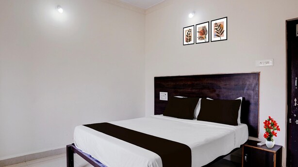 Una habitación de hotel con una cama, una mesita de noche con un florero y tres cuadros colgados en la pared.